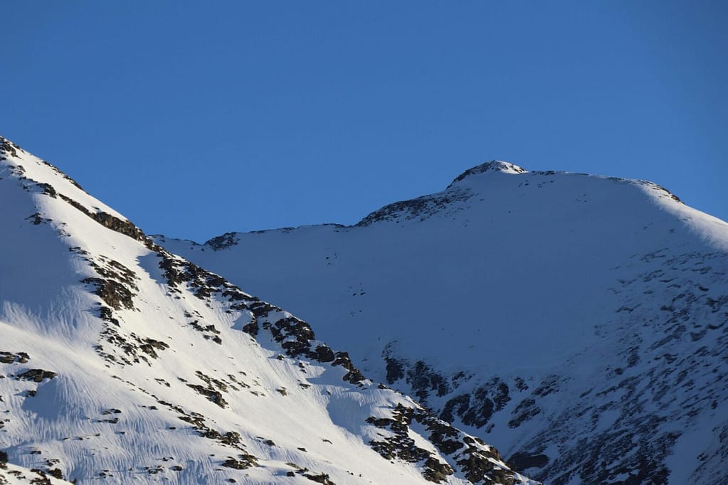 Photo by Henning K. Majestic snow-covered peaks in Andorra under a bright blue sky, showcasing a pristine winter landscape.